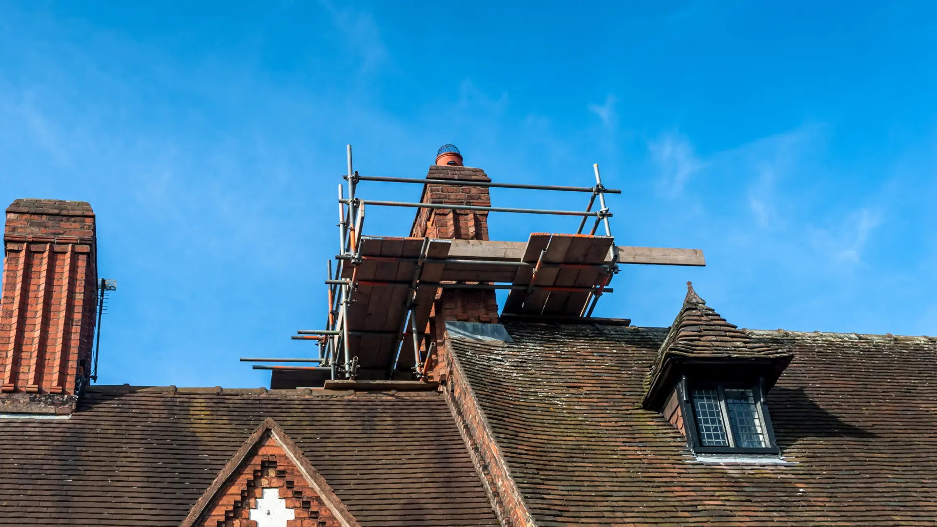 Brick chimney surrounded by scaffolding above a tiled roof
