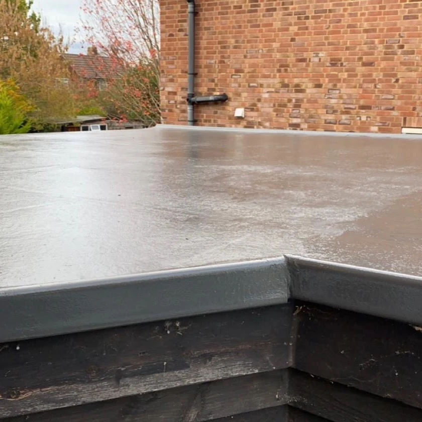 Flat roof surface and edge detail beside a brick wall