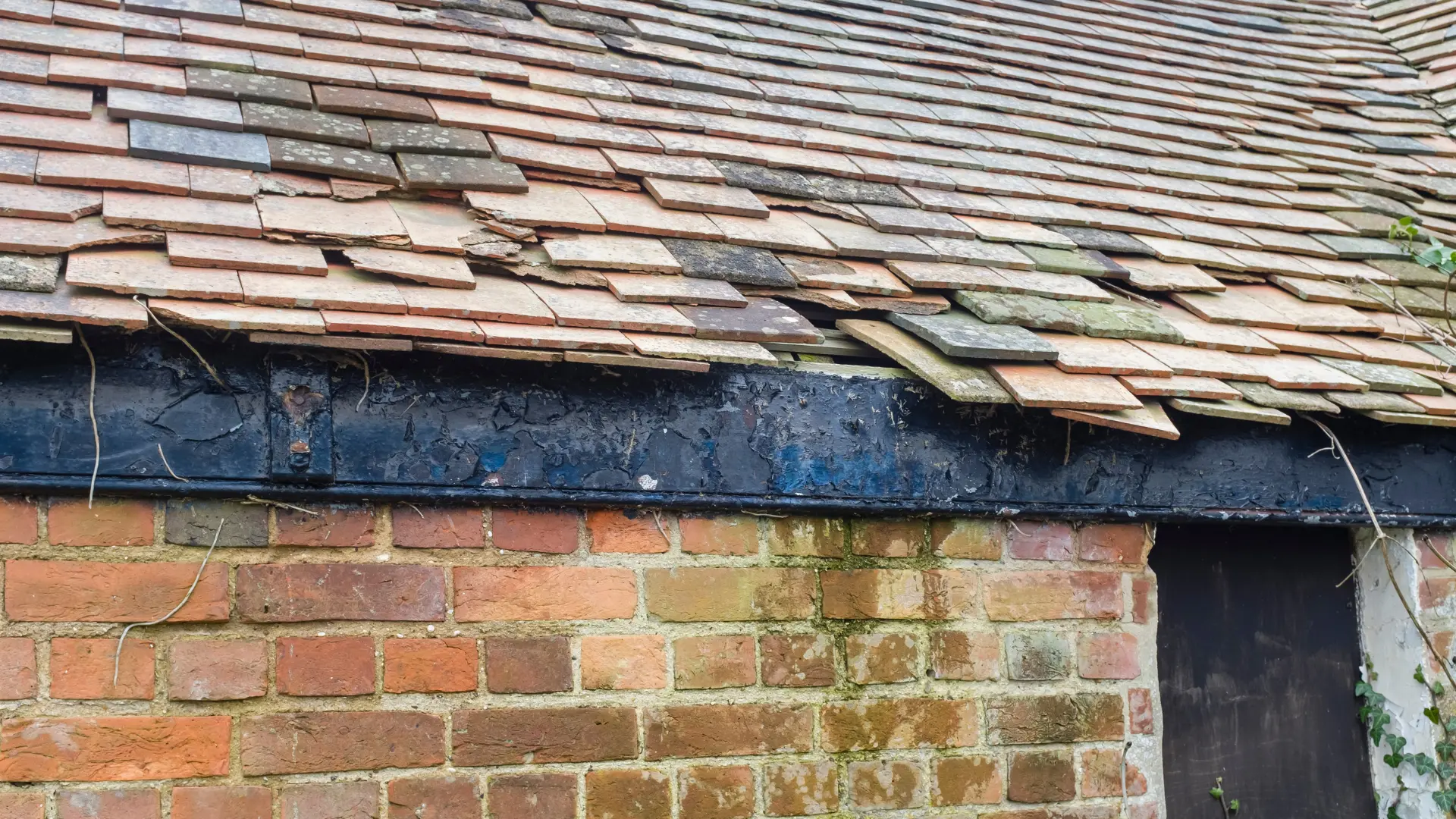 Damaged roof tiles and exposed roof edge above brickwork