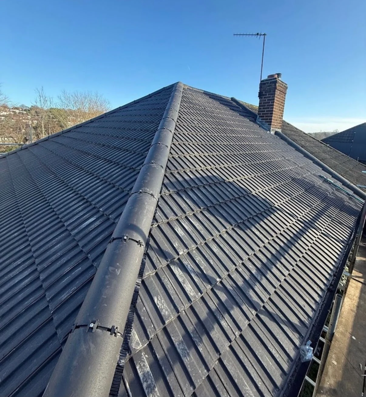 Dark tiled roof slopes meeting at a ridge beside a chimney