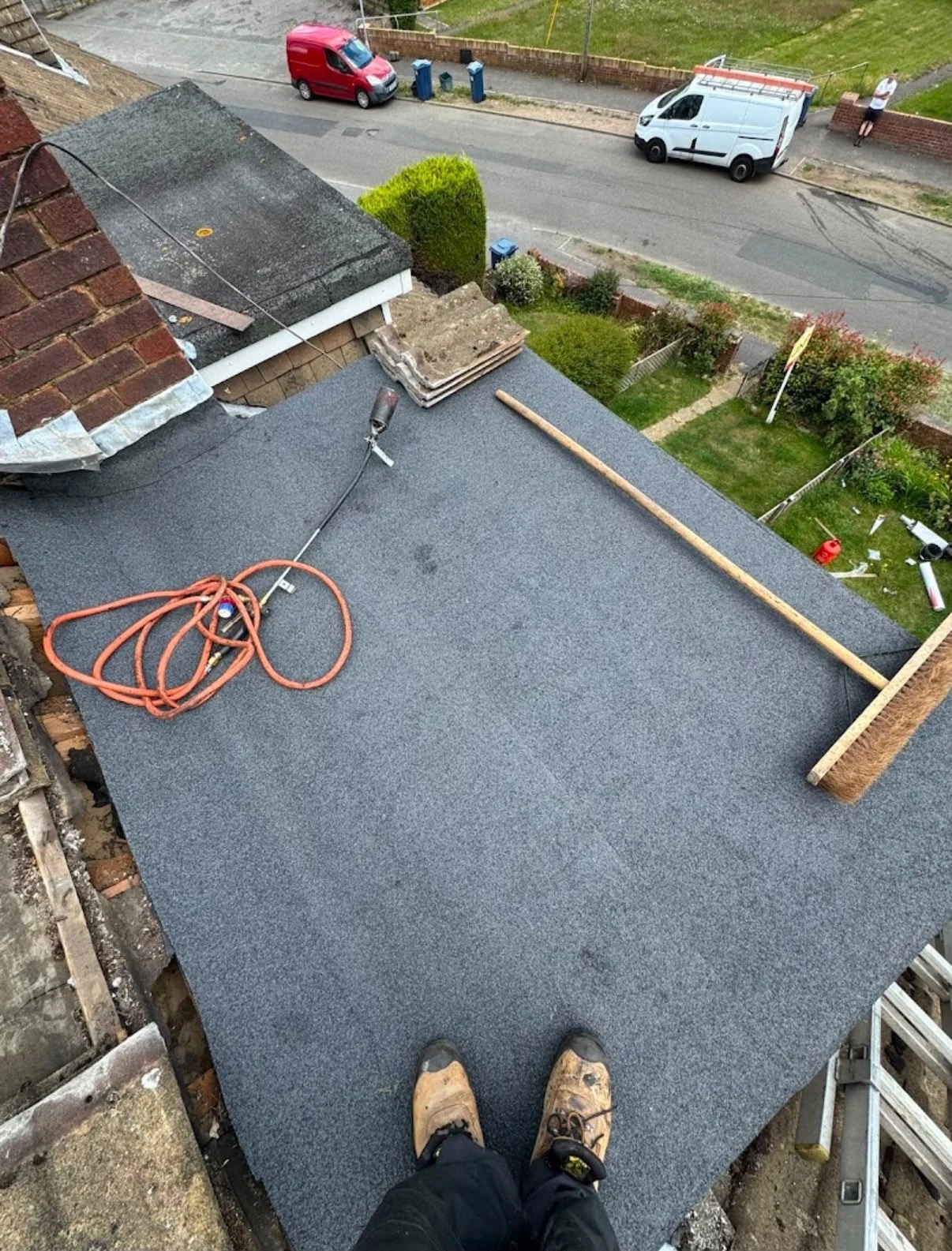 Flat roof covering beside a chimney with a hose and access ladder