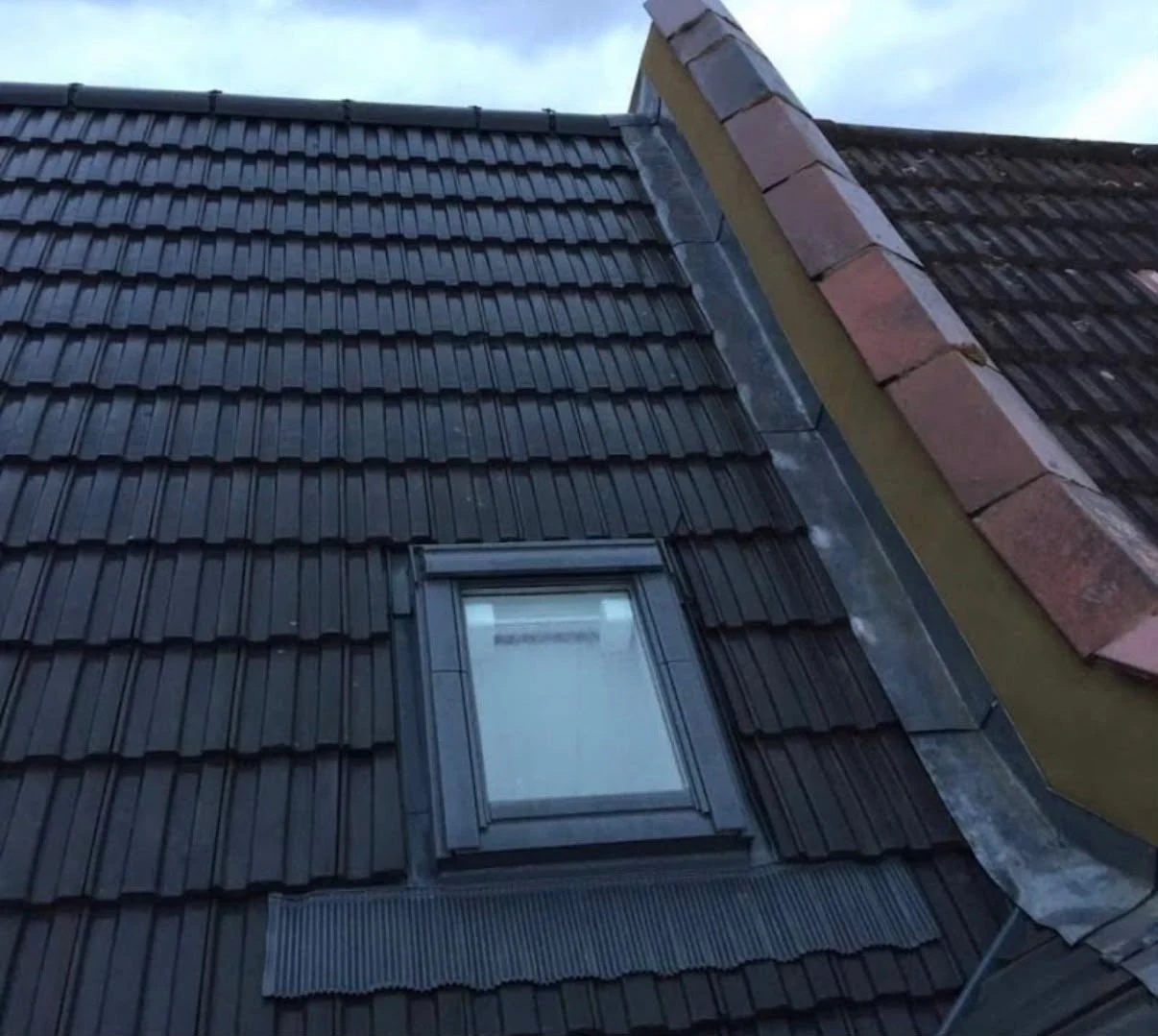 Dark tiled pitched roof with a roof window and ridge tiles