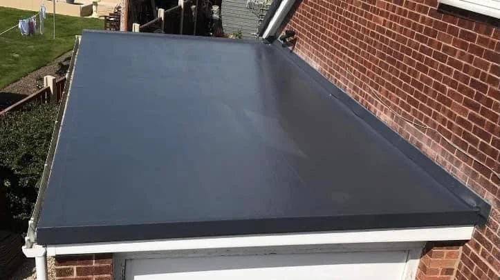 Dark flat roof covering on a small extension beside brickwork